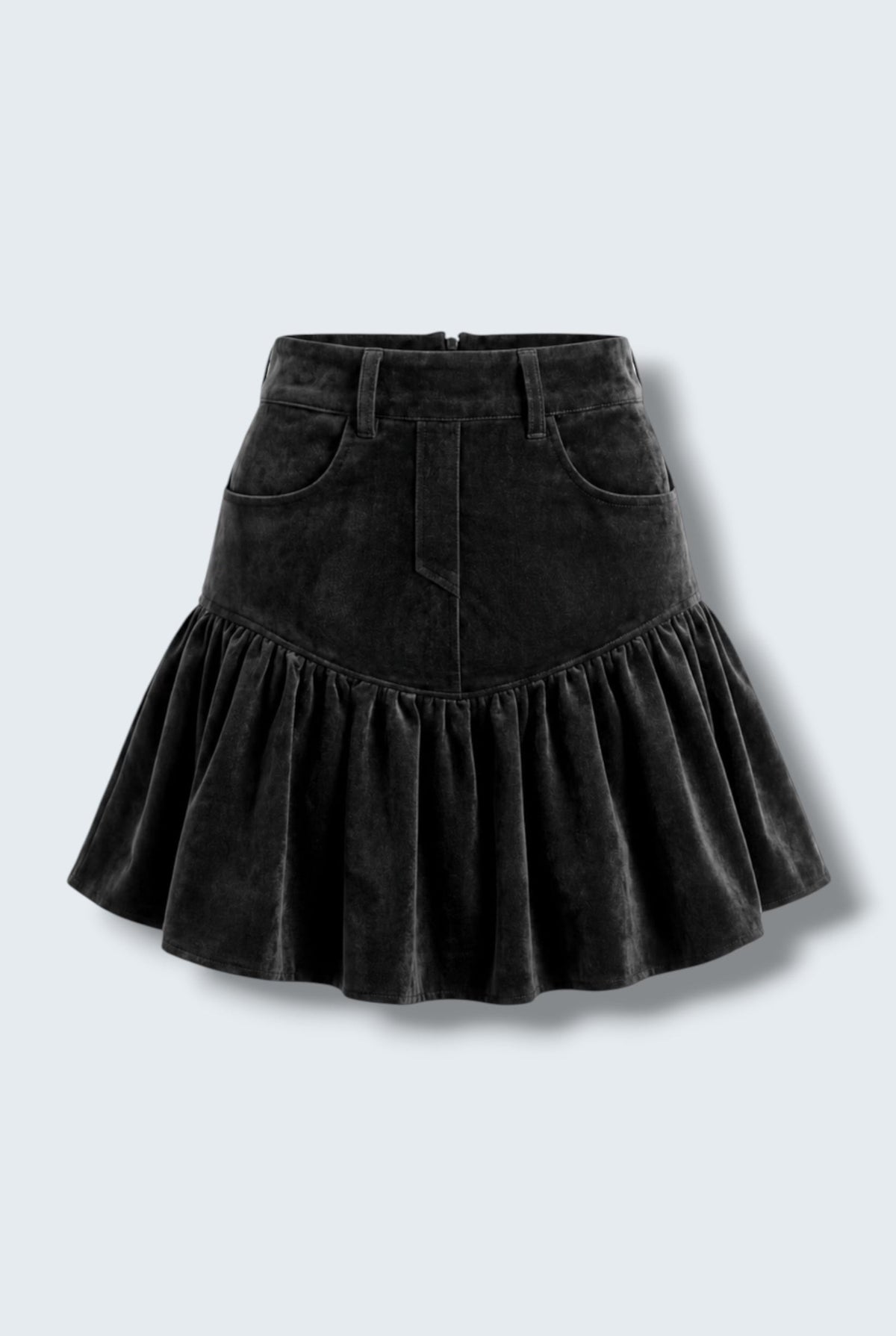 Model wearing The Saint 54 black suede skirt with a high waist, gathered volume, and ruffles, seated on a white block.