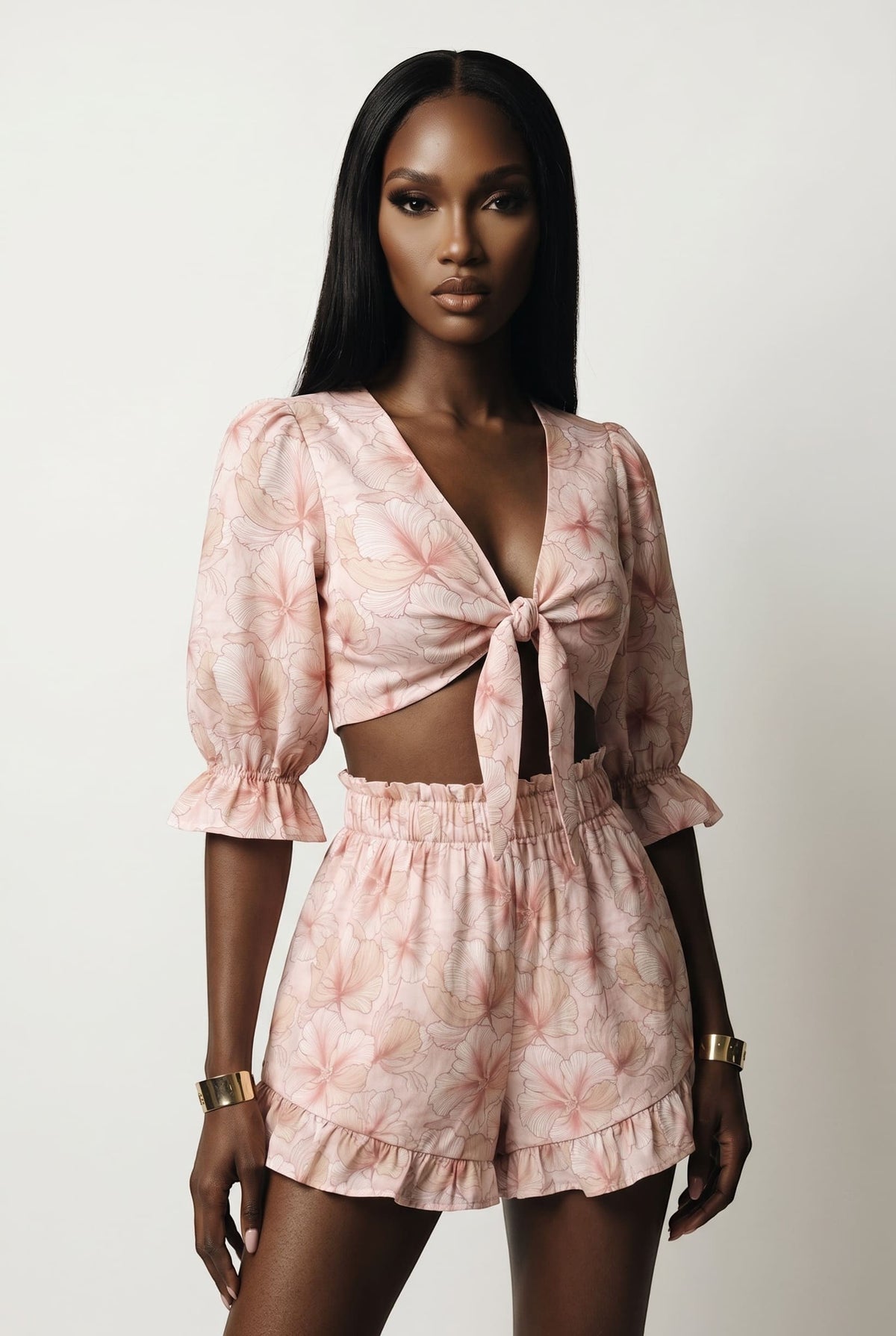 Model wearing The Saint 54 pink floral two-piece set with tie-front puff sleeve top and ruffled high-waisted shorts.